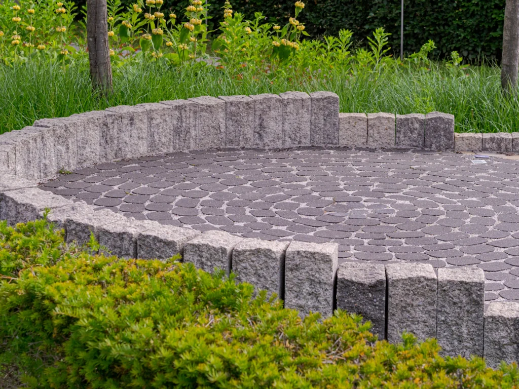 Round paver patio with a low stone wall and shrubs