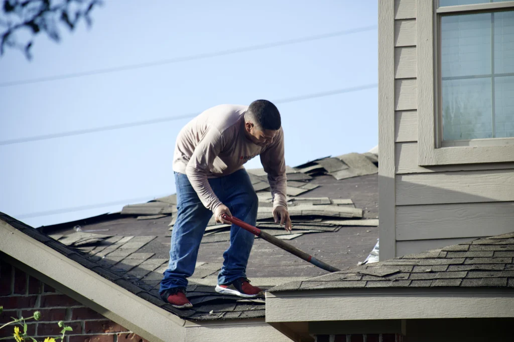 Roofer removing damaged shingles to expose the roof deck